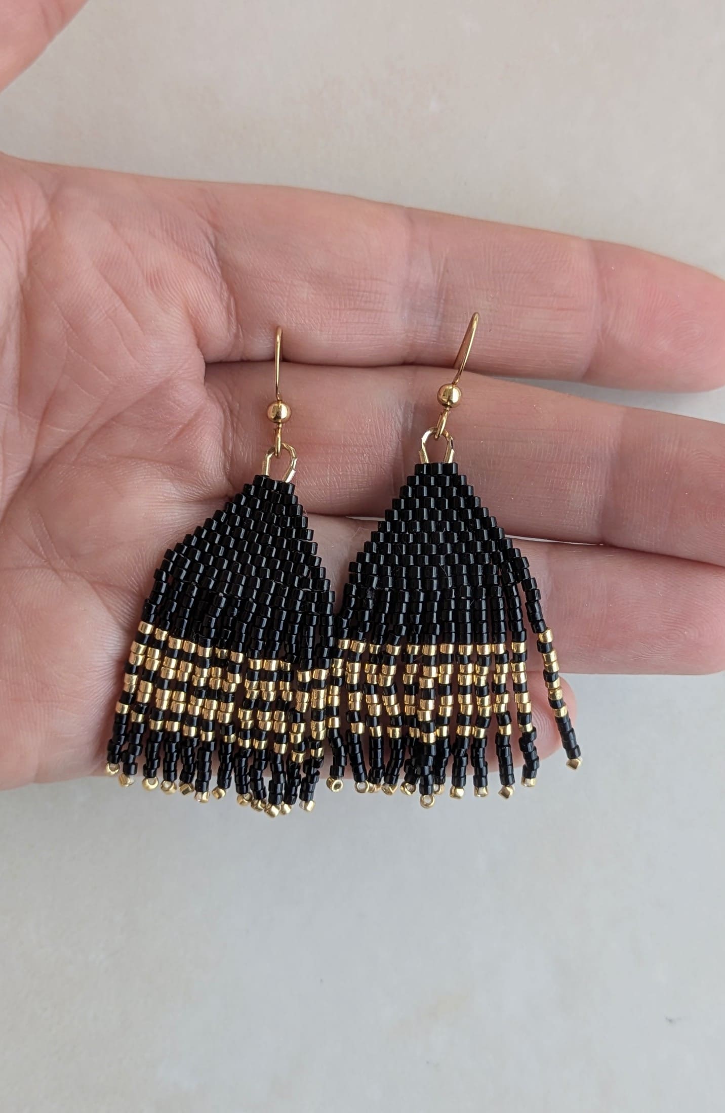 Boucles à franges perlées noires et dorées présentées dans une main
