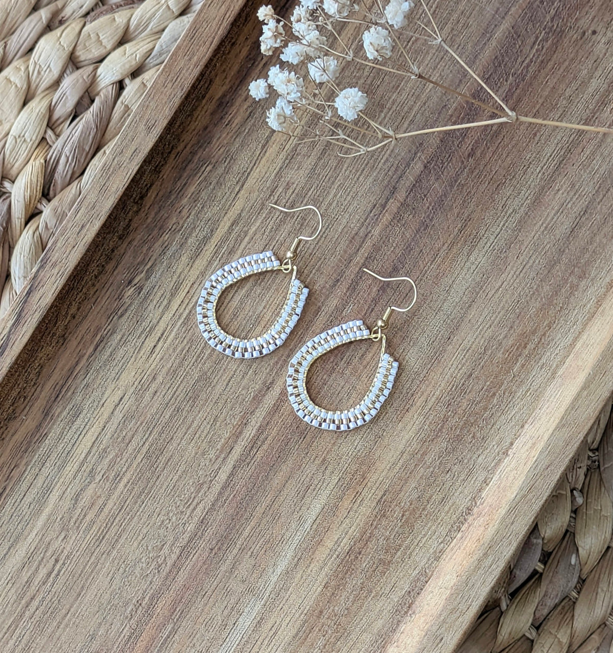 Boucles d'oreilles en perles blanches et dorées tissées sur un anneau doré en forme de goutte. Décor bohème.
