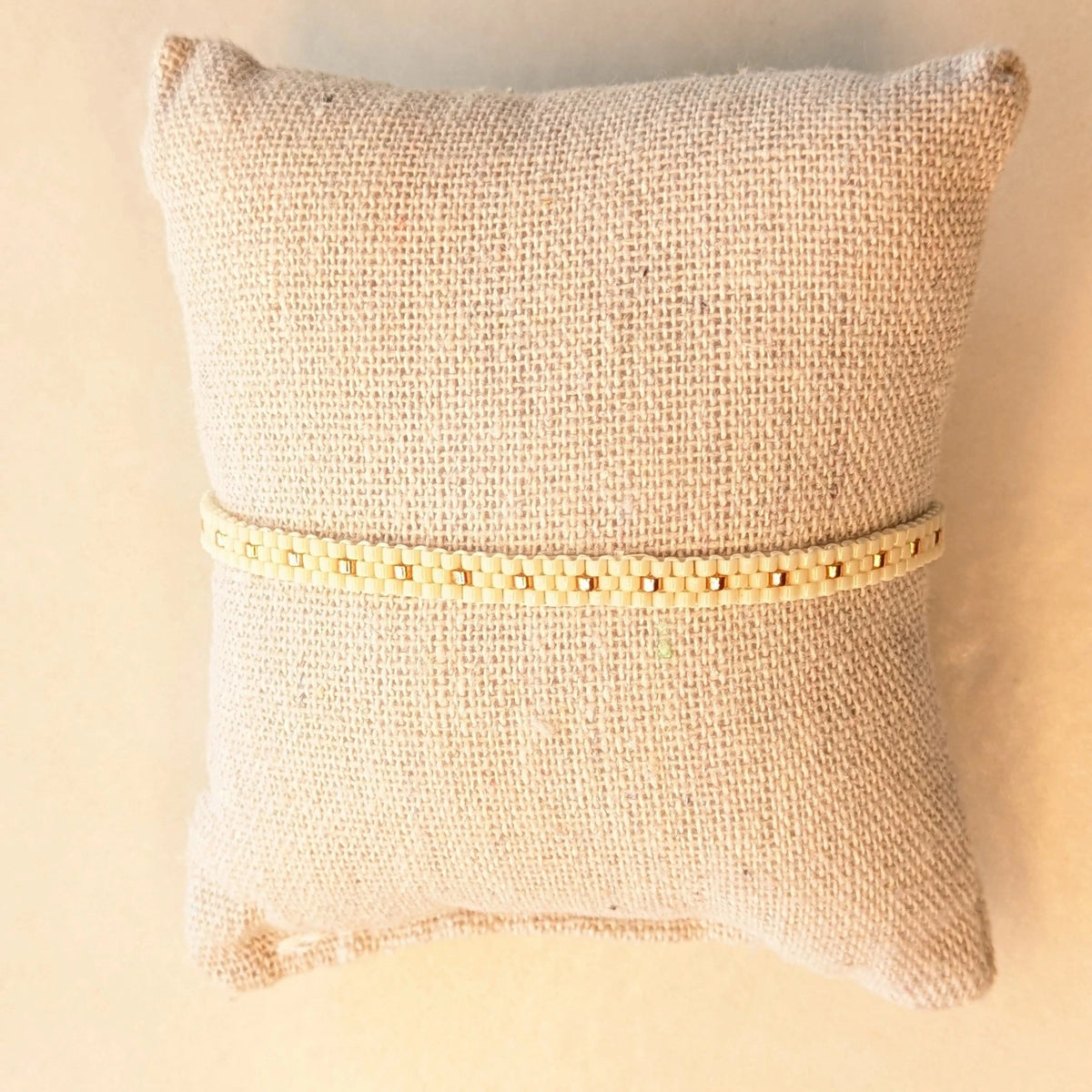 Bracelet tissé fin crème présenté sur coussin