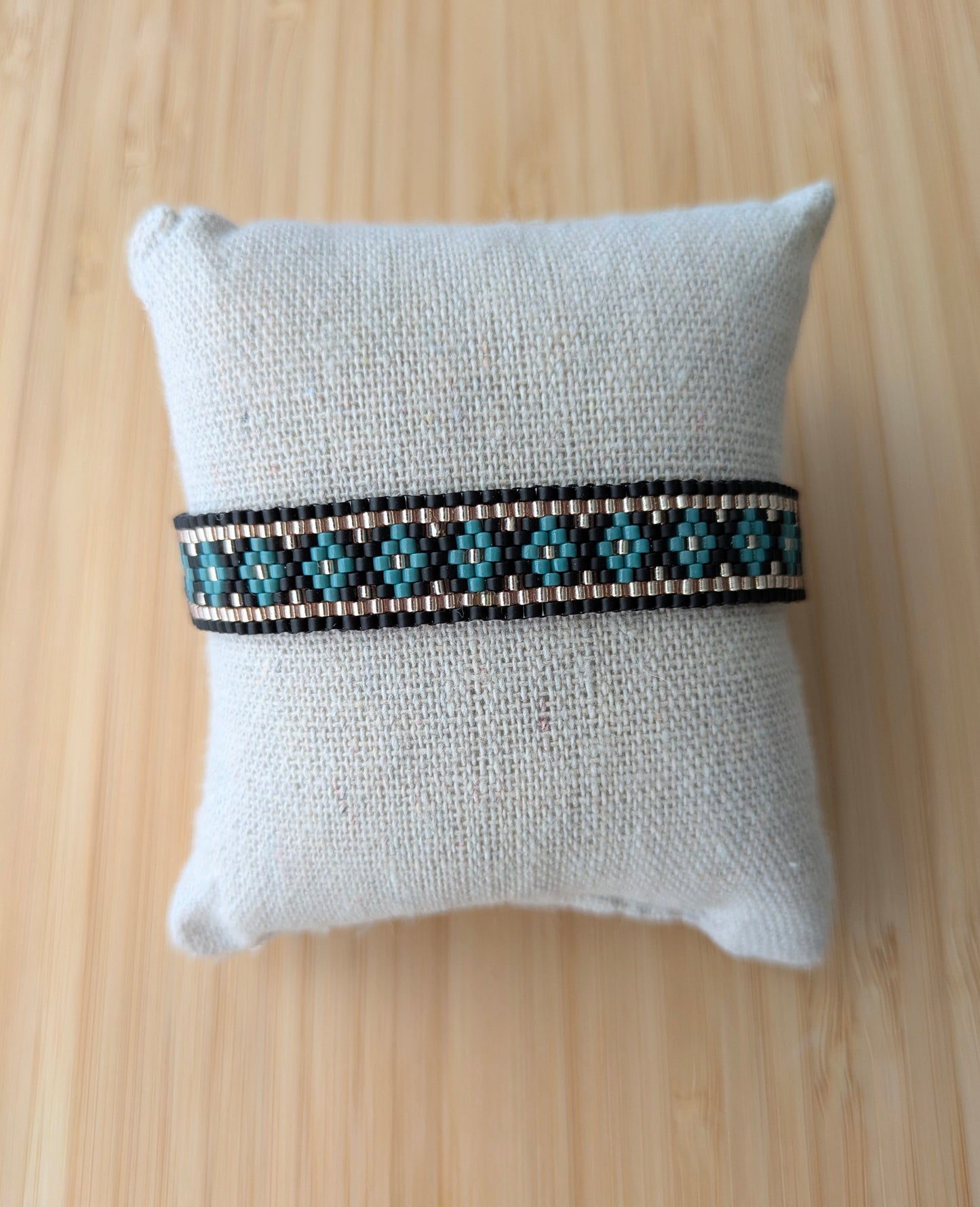 Bracelet fait-main en perles miyuki noires et vertes présenté sur un coussin