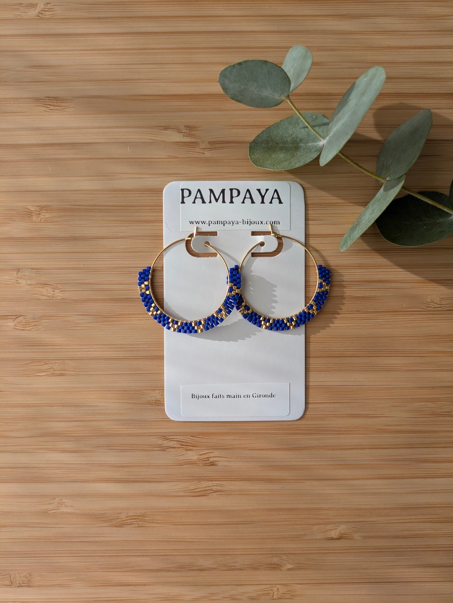 Créoles bleues et dorées sur présentoir bijoux à plat sur planche en bambou - Bijou en perles tissées main