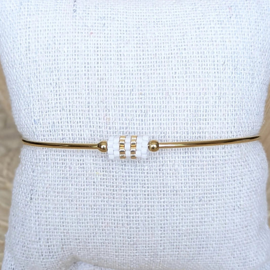 Vue détaillée du bracelet jonc doré avec tissage de perles blanches - Présenté sur un coussin