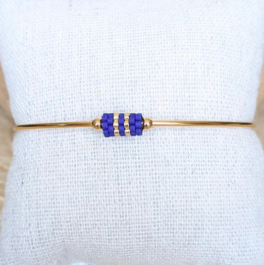 Gros plan sur bracelet jonc doré orné d'un tissage de perles bleues - Bijou présenté sur un coussin
