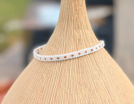 Bracelet tissé main en perles miyuki blanches et cuivrées sur un vase