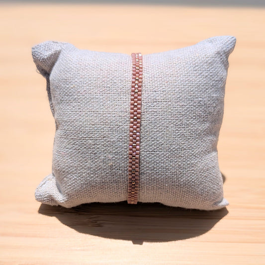 bracelet rose et argenté en perles tissées à la main sur coussin exposé au soleil. Les perles brillent.
