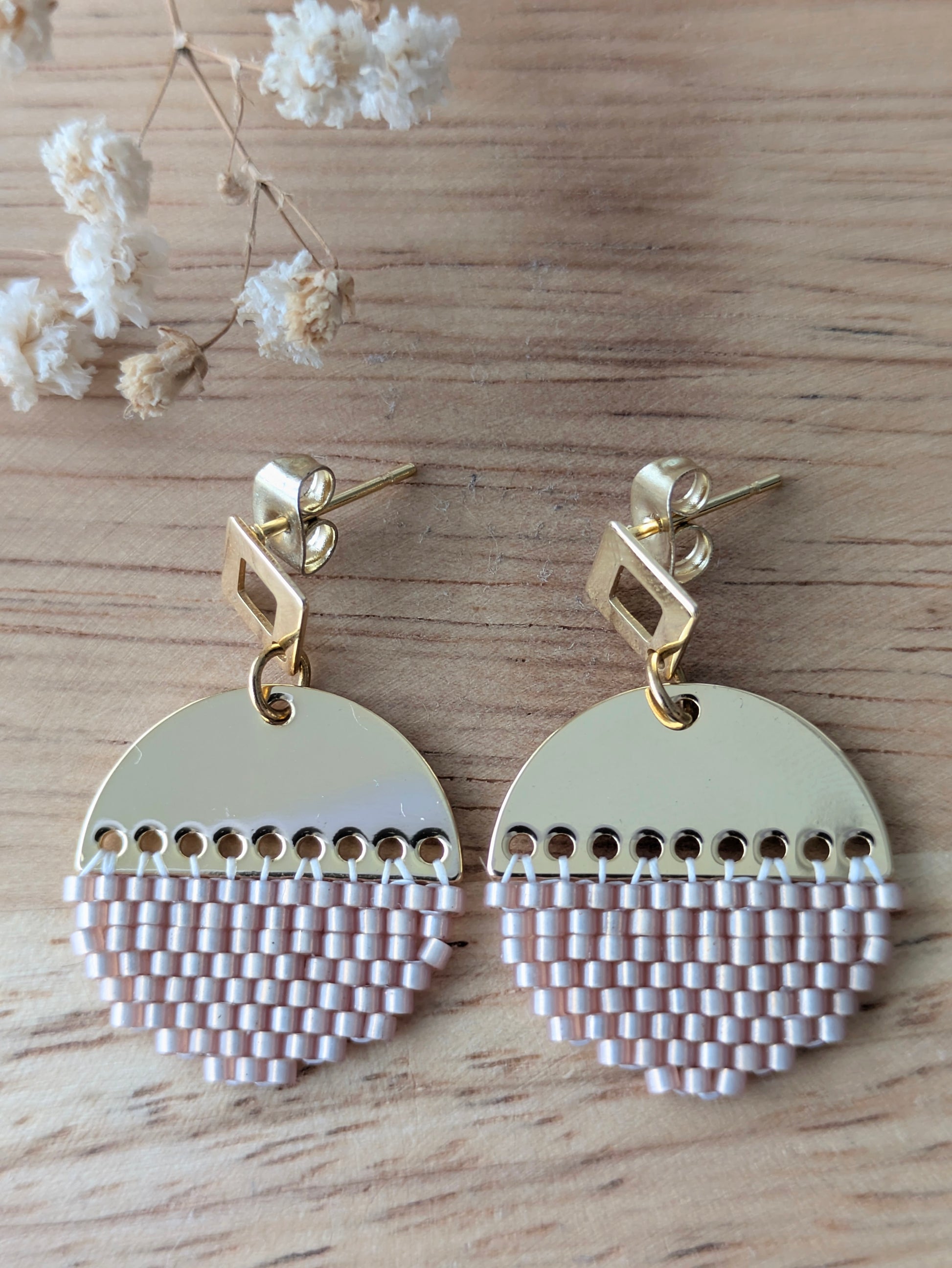 Gros plan sur les boucles artisanales LUNA de couleur beige rosé avec puces en acier inoxydable doré.