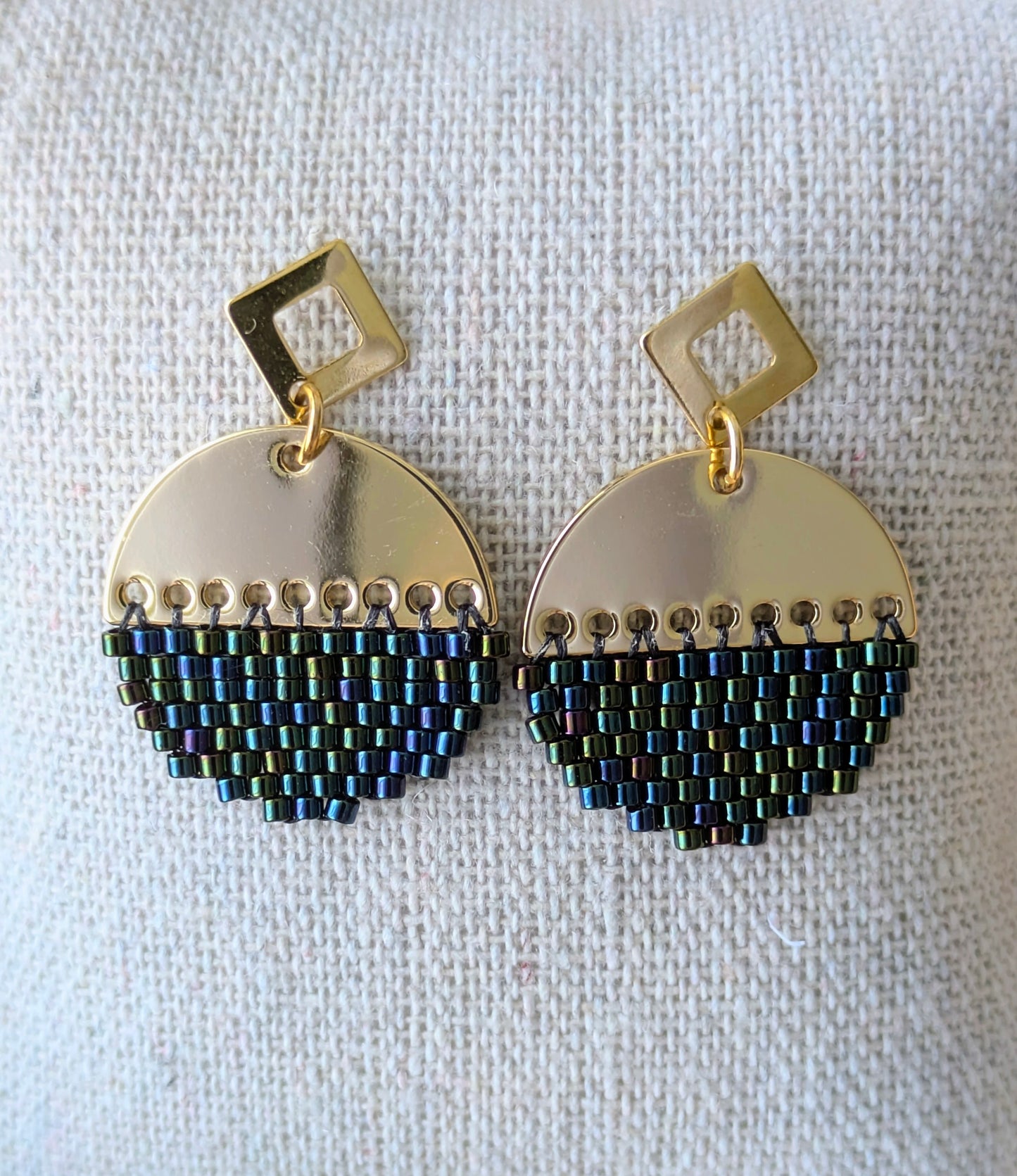 Gros plan sur les boucles rondes en perles tissées avec reflets bleus et verts irisés.