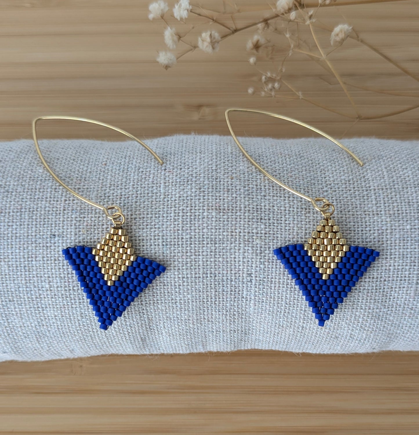 Boucles tissées main en perles bleues et dorées présentées sur un coussin