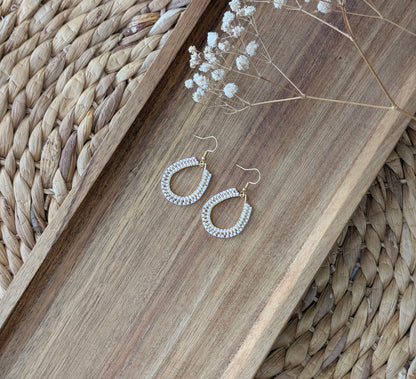 Boucles d'oreilles perlées blanches et dorées style bohème posées sur plat en bois.