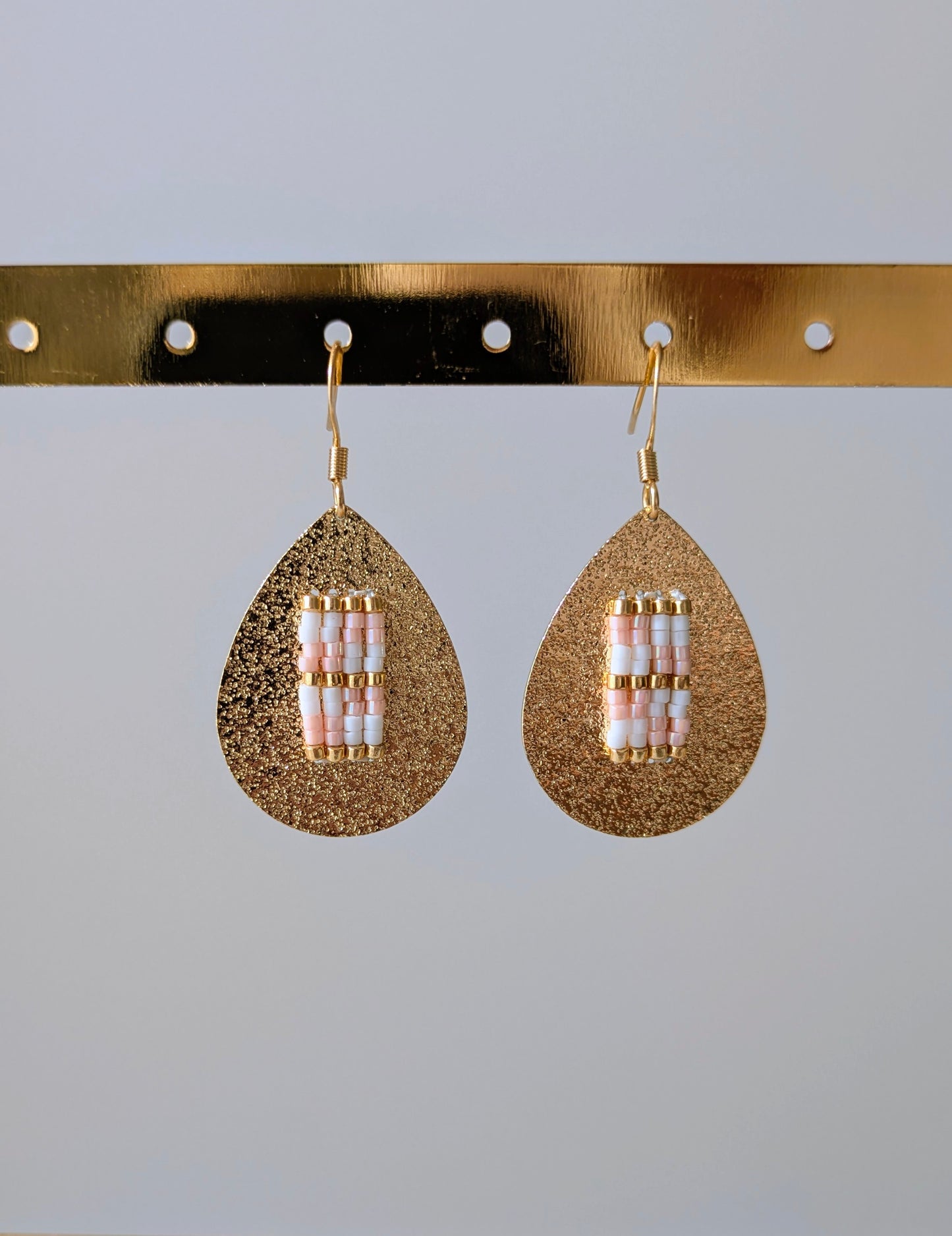 Vue détaillée des boucles d'oreilles tissées blanc et rose sur goutte en laiton doré