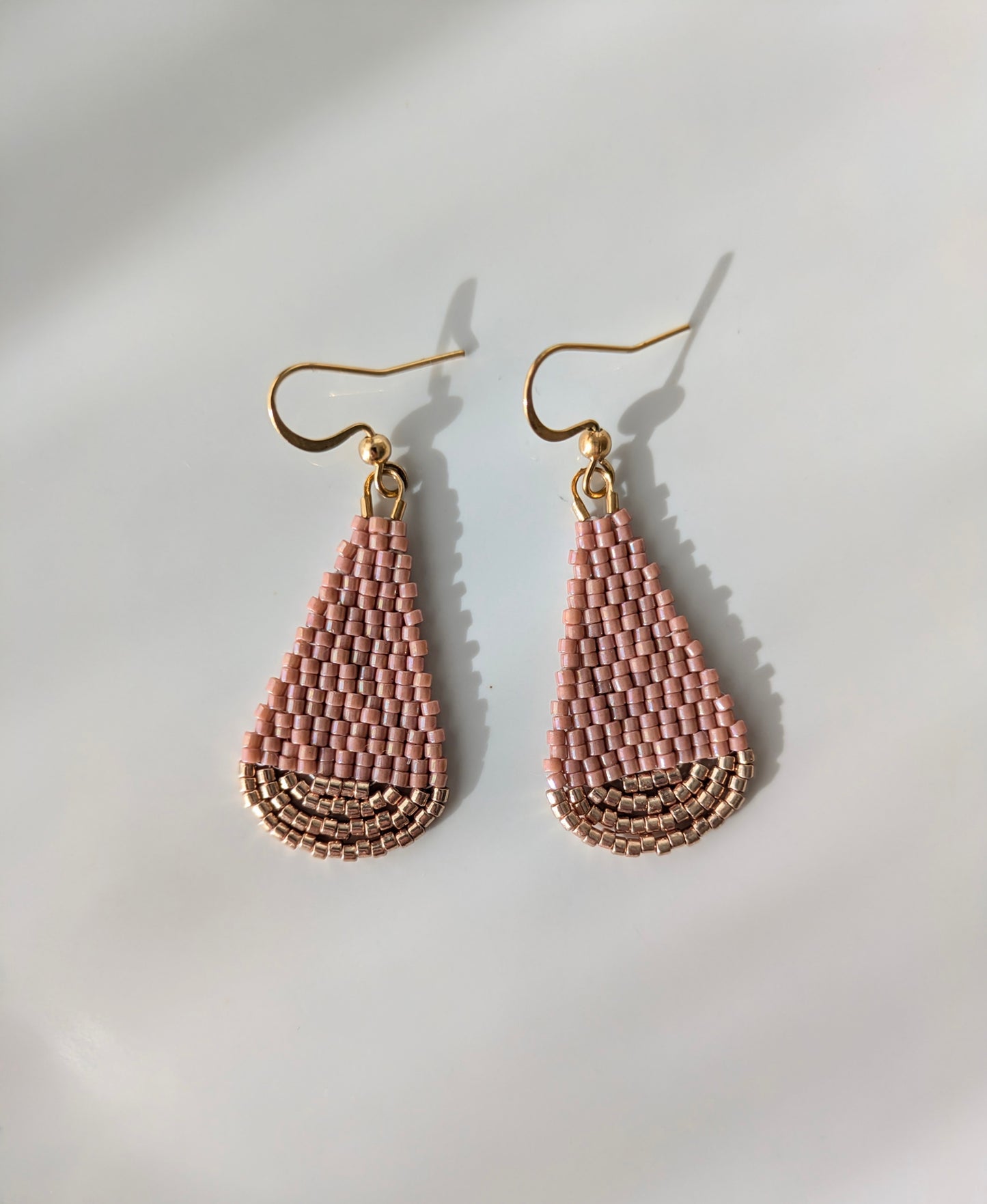 Vue détaillée du tissage artisanal des boucles goutte en perles de verre roses posées à plat