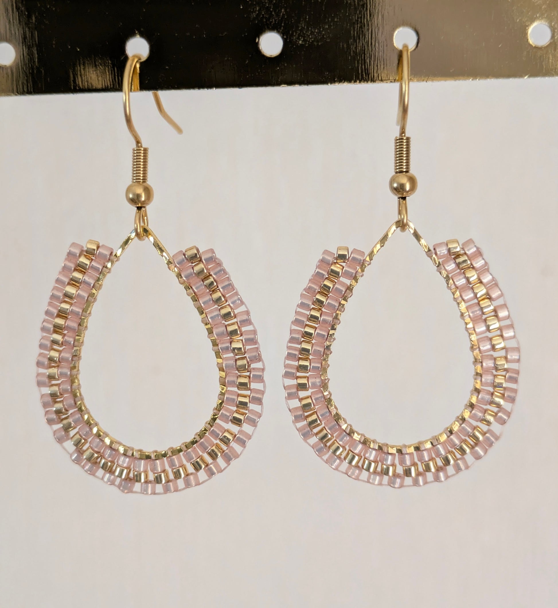 Boucles d'oreilles perlées beiges. Vue détaillée du tissage sur anneau doré en forme de goutte.