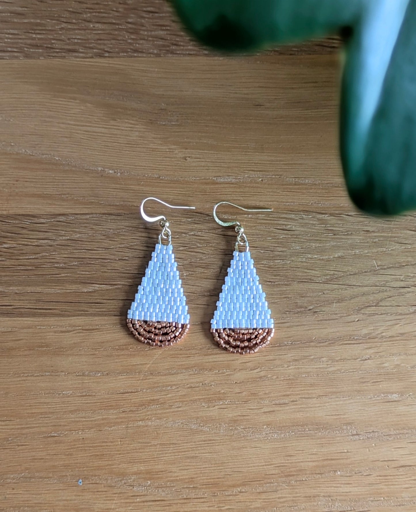 Vue de haut des boucles artisanales en forme de goutte et en perles de verre blanches et cuivrées