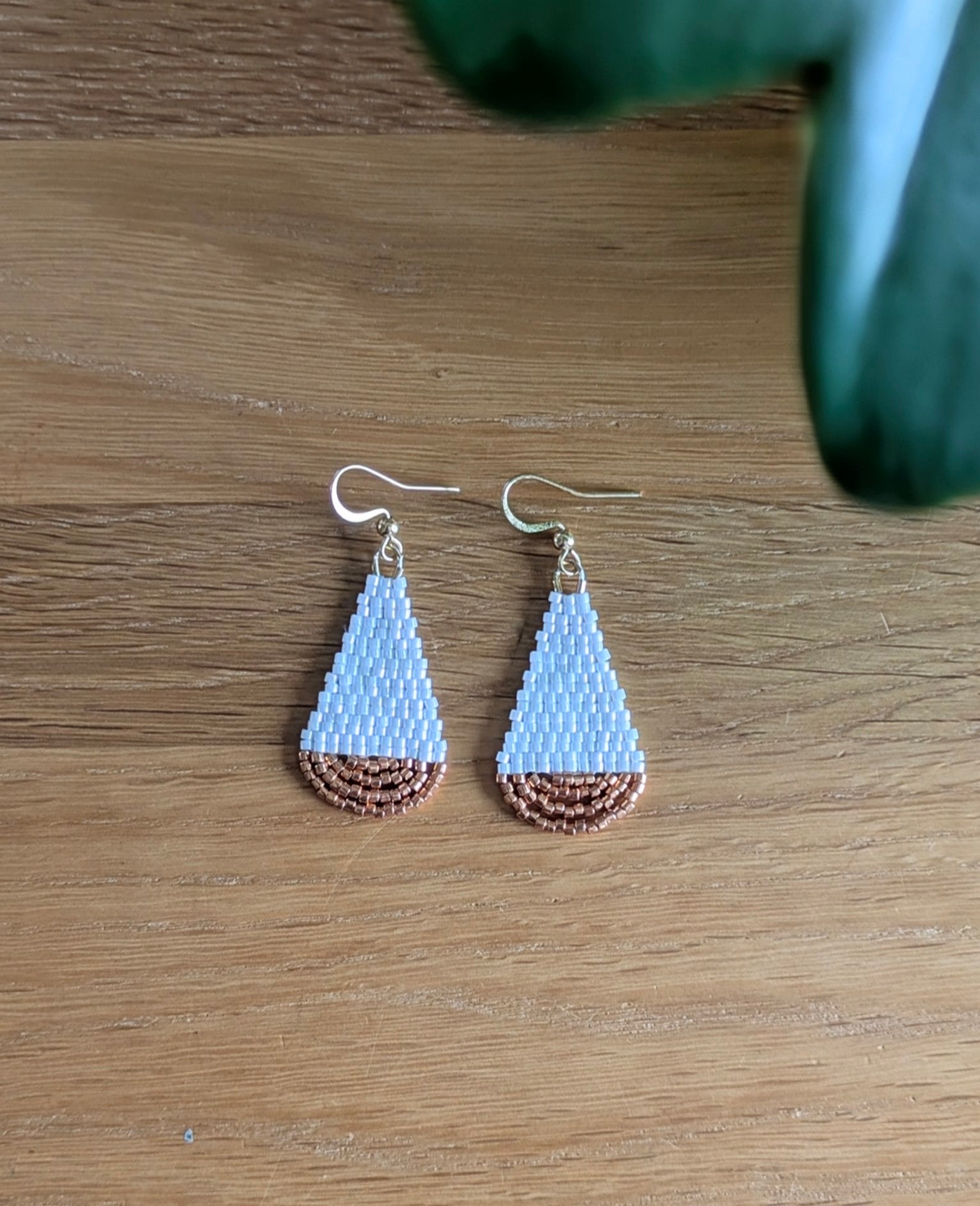 Vue de haut des boucles artisanales en forme de goutte et en perles de verre blanches et cuivrées