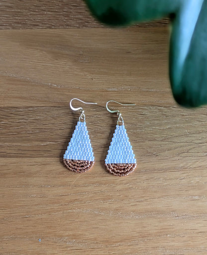 Vue de haut des boucles artisanales en forme de goutte et en perles de verre blanches et cuivrées