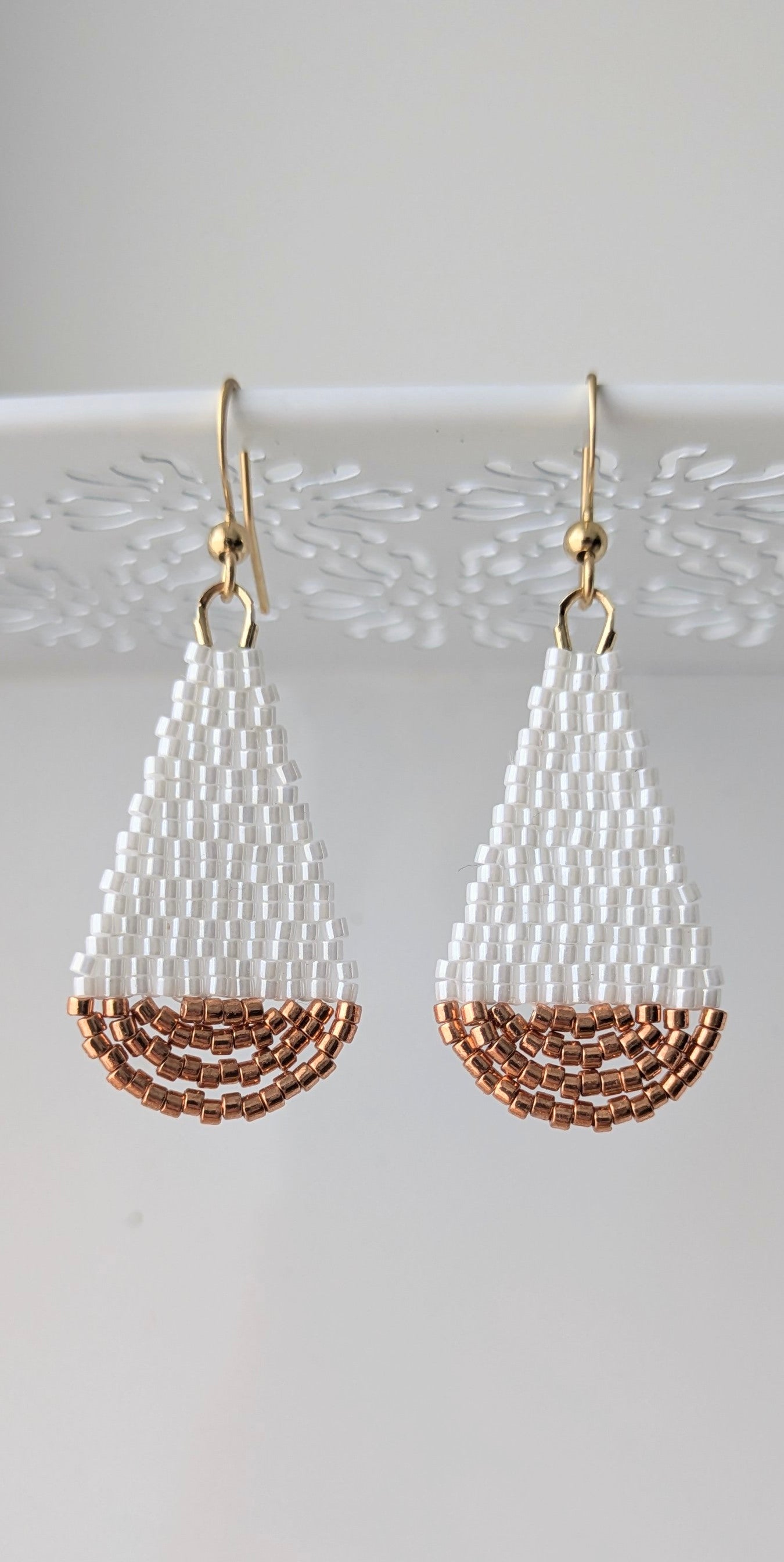 Gros plan sur le tissage artisanal des boucles goutte en perles blanches et cuivrées