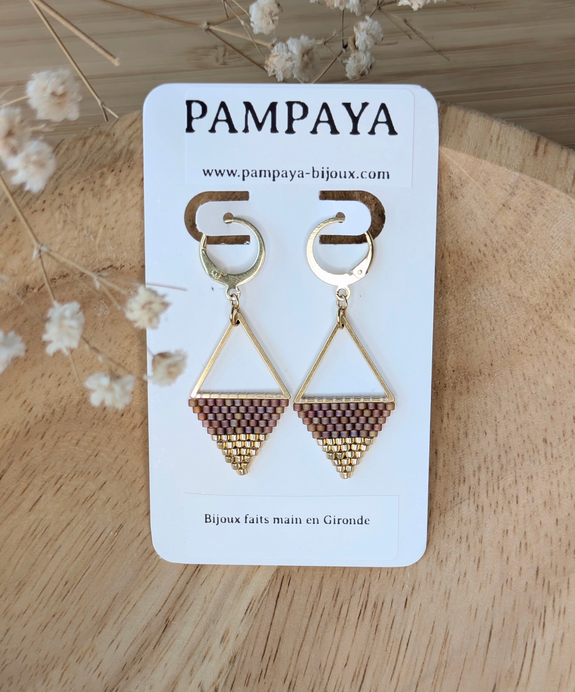 Boucles tissées main rouges et dorées sur triangle sur présentoir indiquant "Pampaya-bjoux faits main en gironde"
