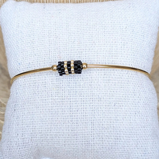 Bracelet jonc doré avec tissage de perles noires présenté sur coussin - Vue de face