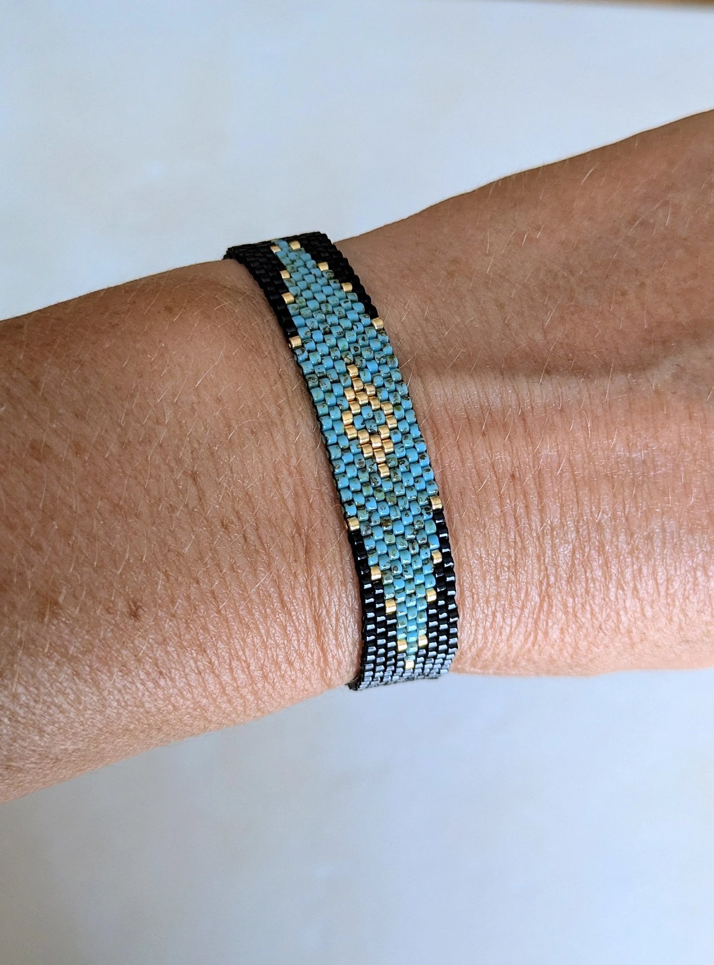 Bracelet Horizon en perles turquoises, noires et dorées porté sur poignet féminin