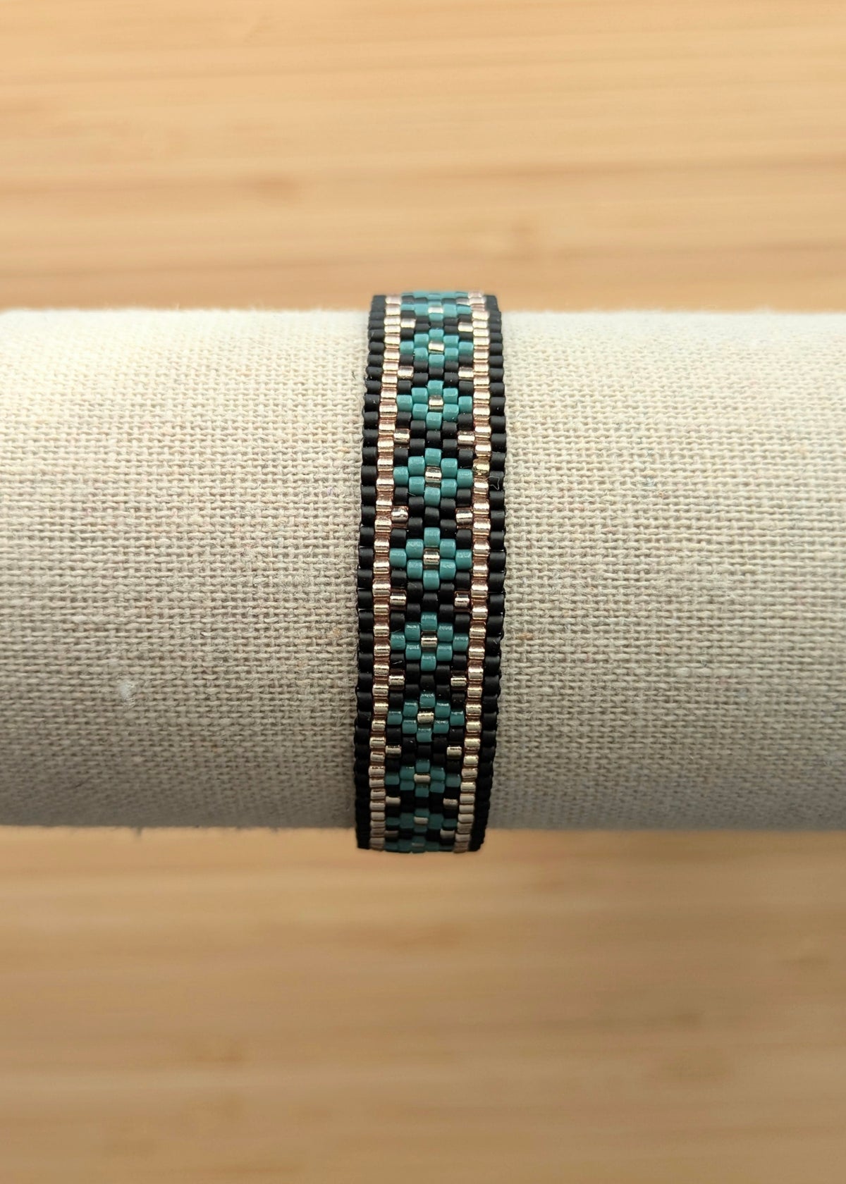 Bracelet tissé en perles de verre noires et vertes sur présentoir. Bijou artisanal