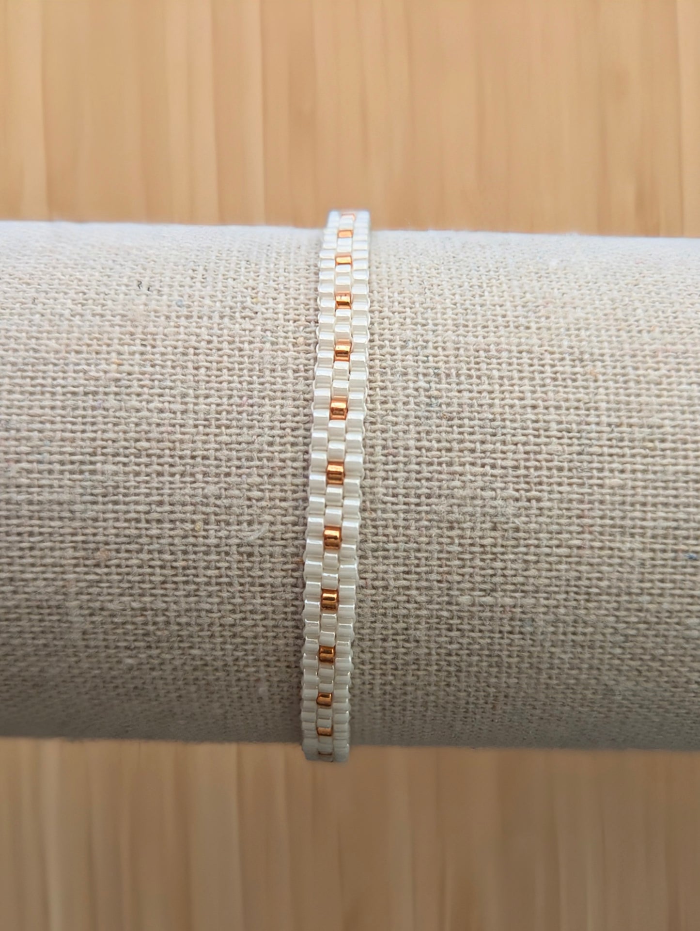Gros plan sur bracelet fin tissé main en perles blanches et cuivrées sur présentoir