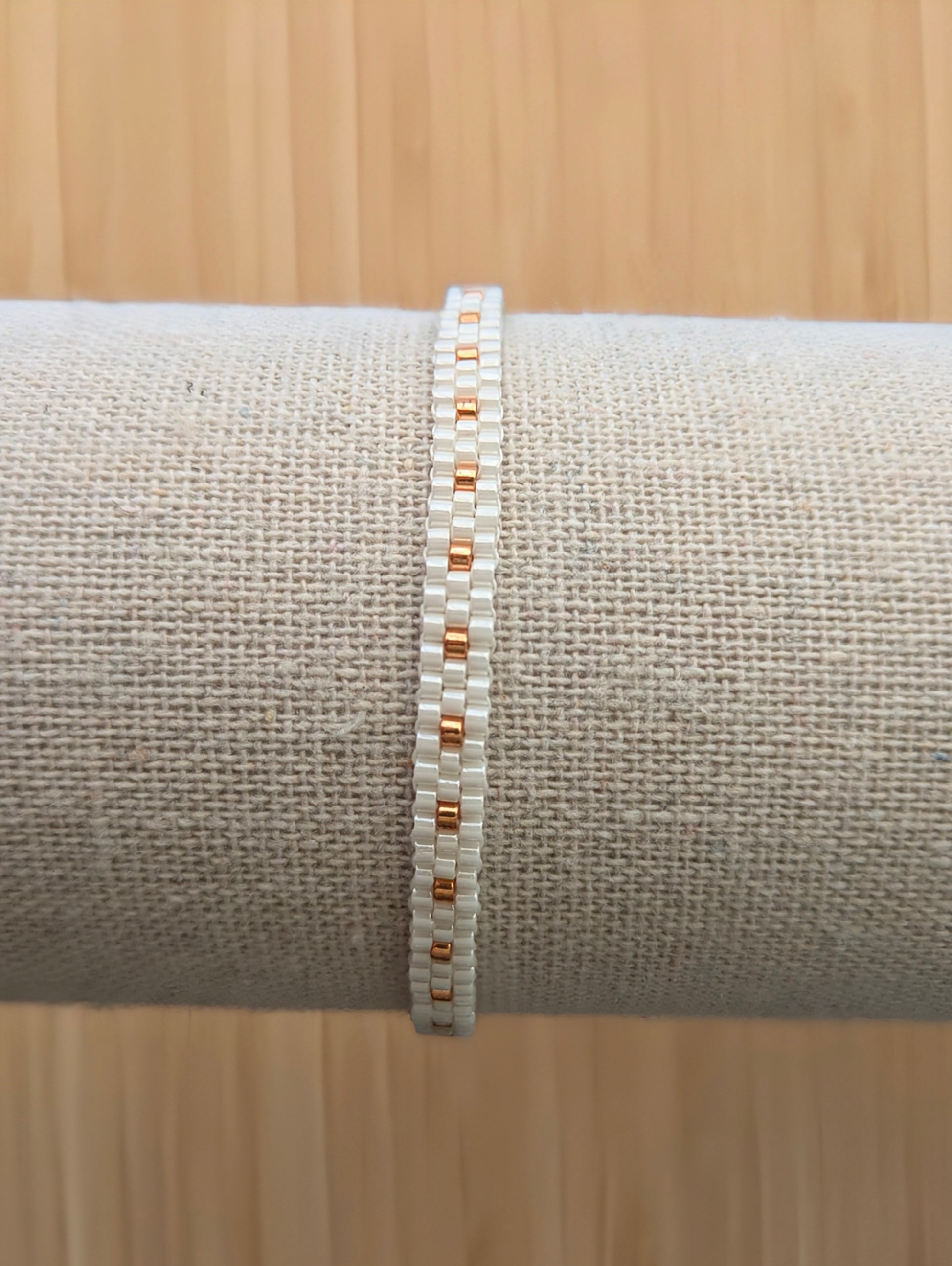 Gros plan sur bracelet fin tissé main en perles blanches et cuivrées sur présentoir