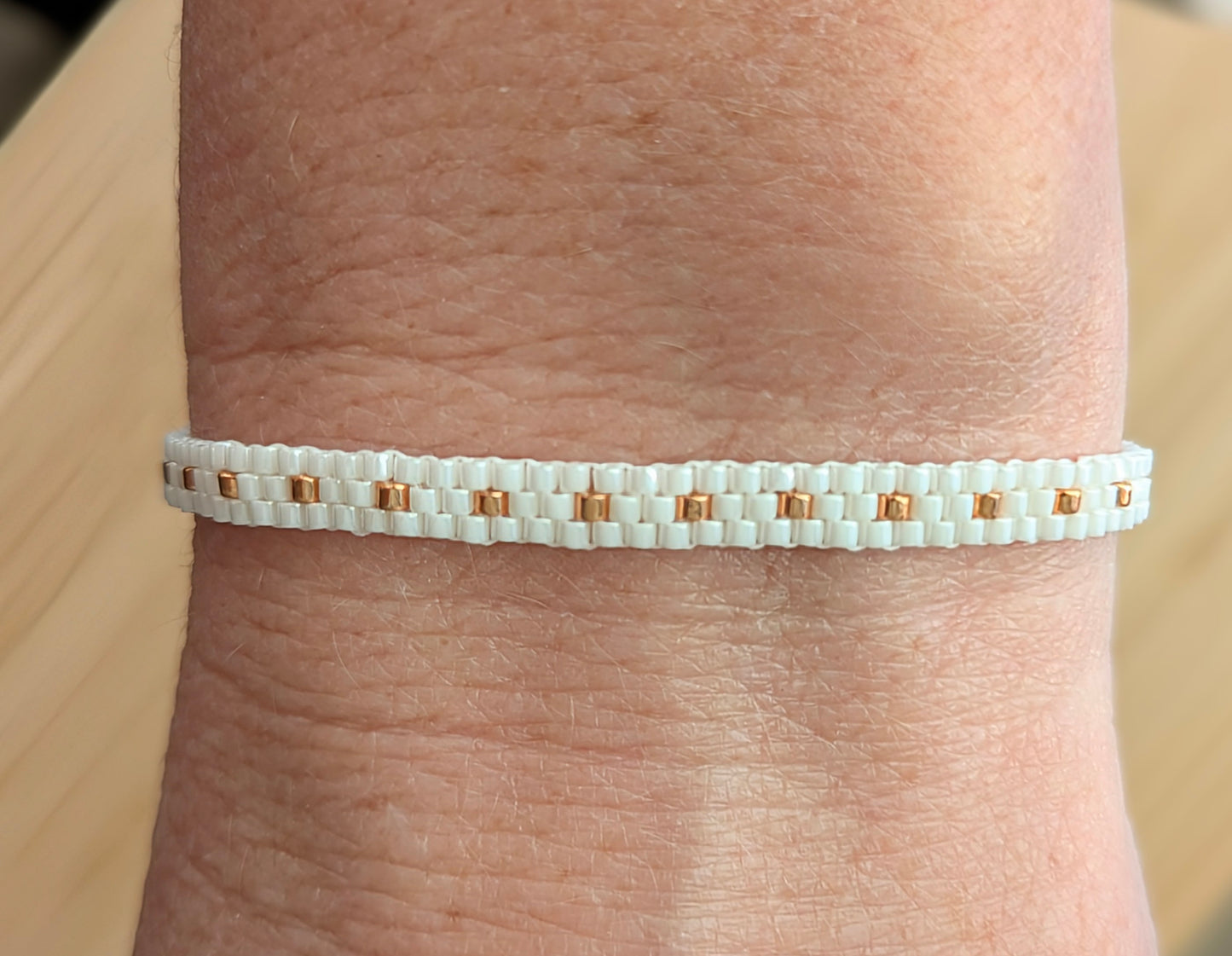 Vue détaillée du tissage du bracelet en perles miyuki blanches et cuivrées porté sur poignet féminin