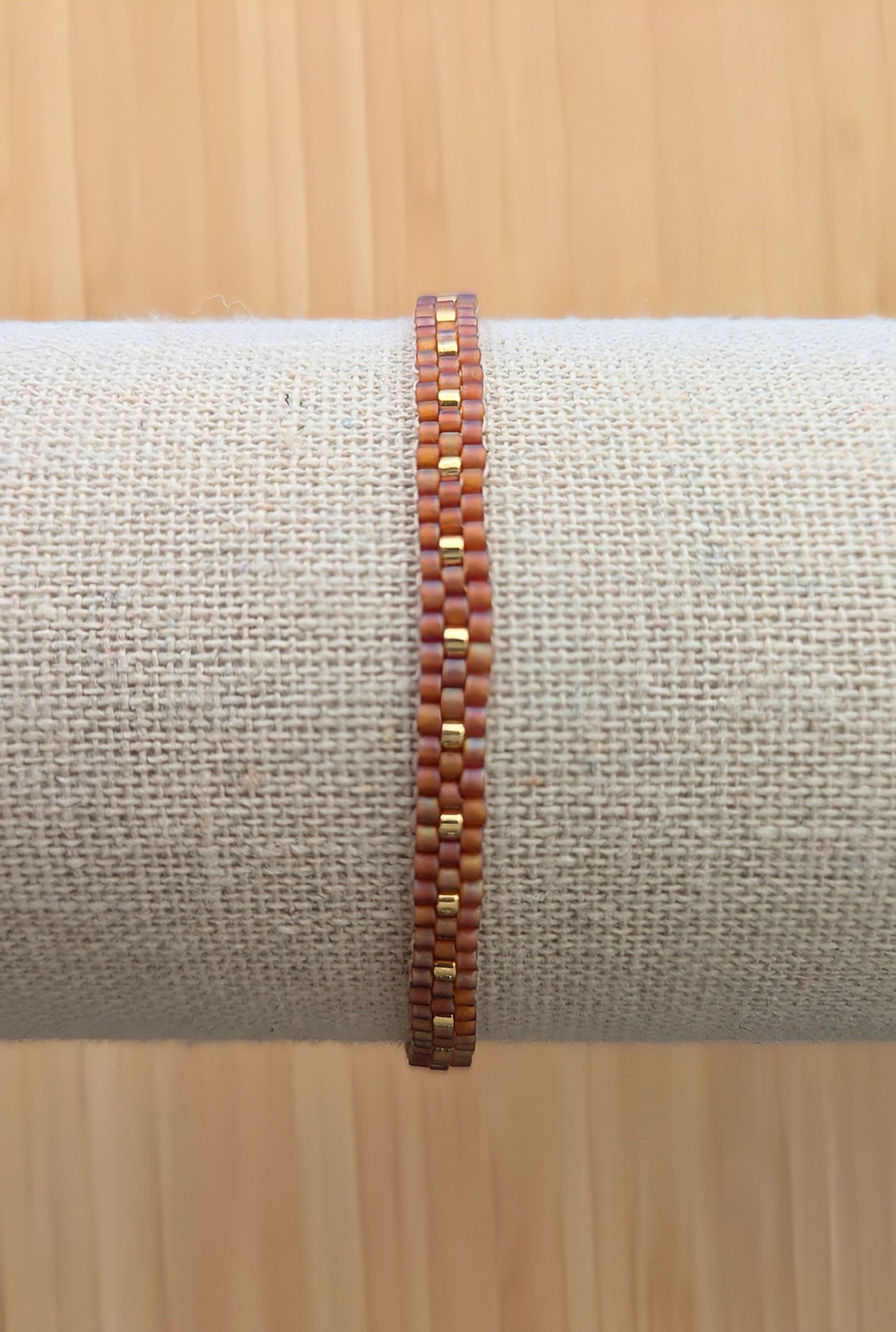 Vue détaillée du tissage des perles rouges et dorées du bracelet fin sur un présentoir