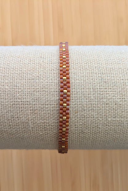 Vue détaillée du tissage des perles rouges et dorées du bracelet fin sur un présentoir