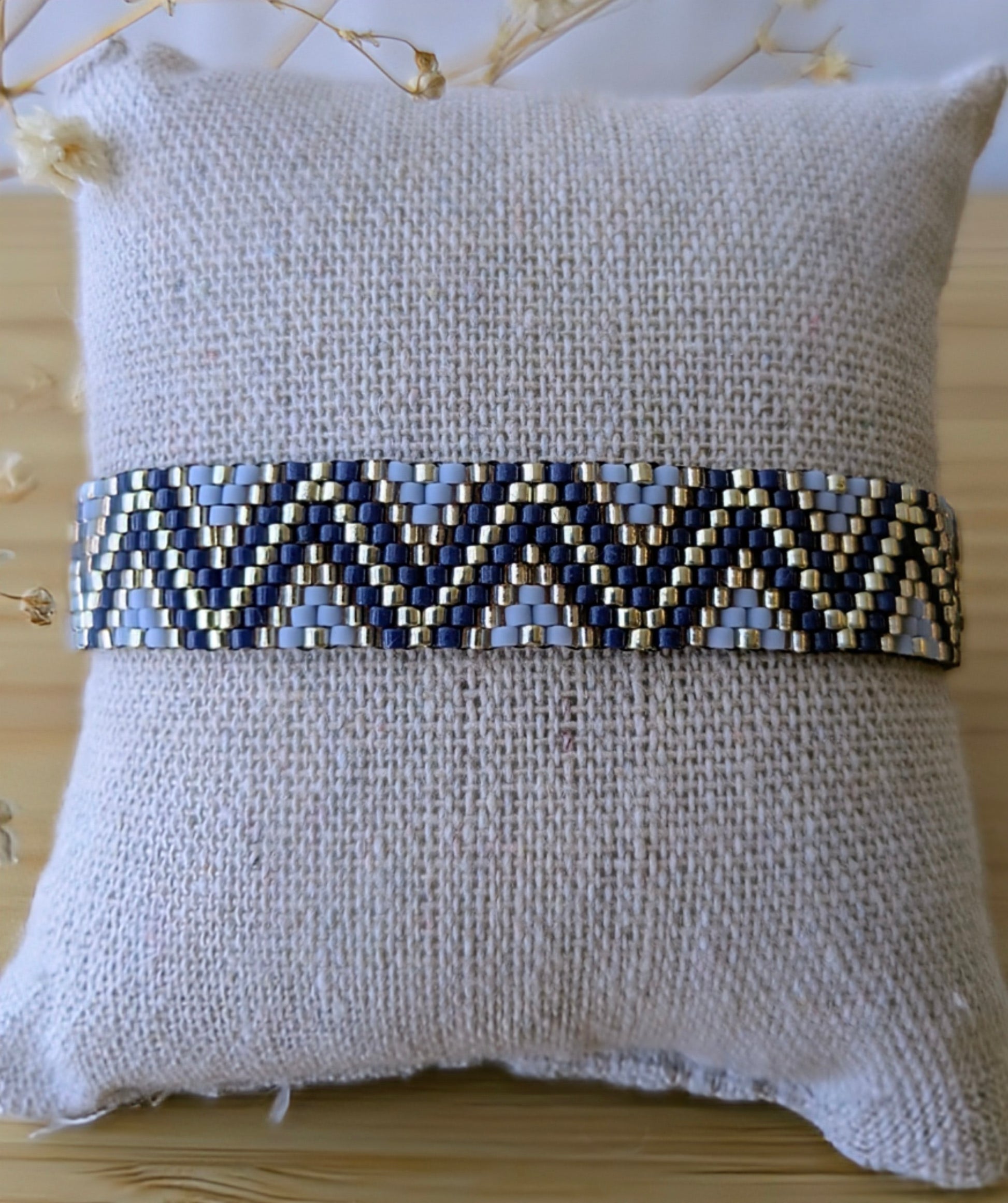 Bracelet avec motifs en zigzag et perles bleues et argent tissé à la main présenté sur un coussin de couleur gris clair.