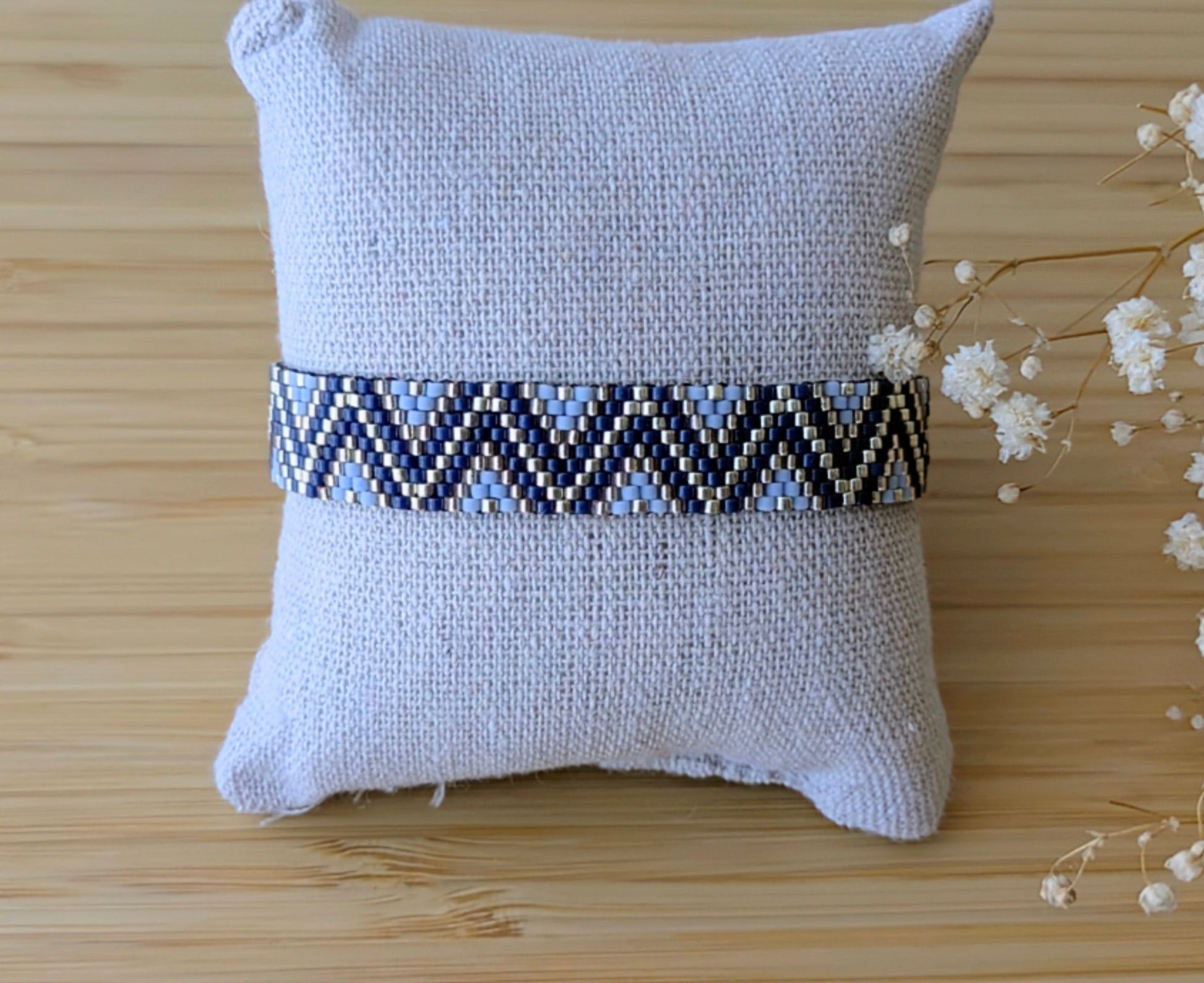 Bracelet en tissage peyote fait main en gironde avec des perles miyuki bleues et argentées. Bijou posé sur un coussin.