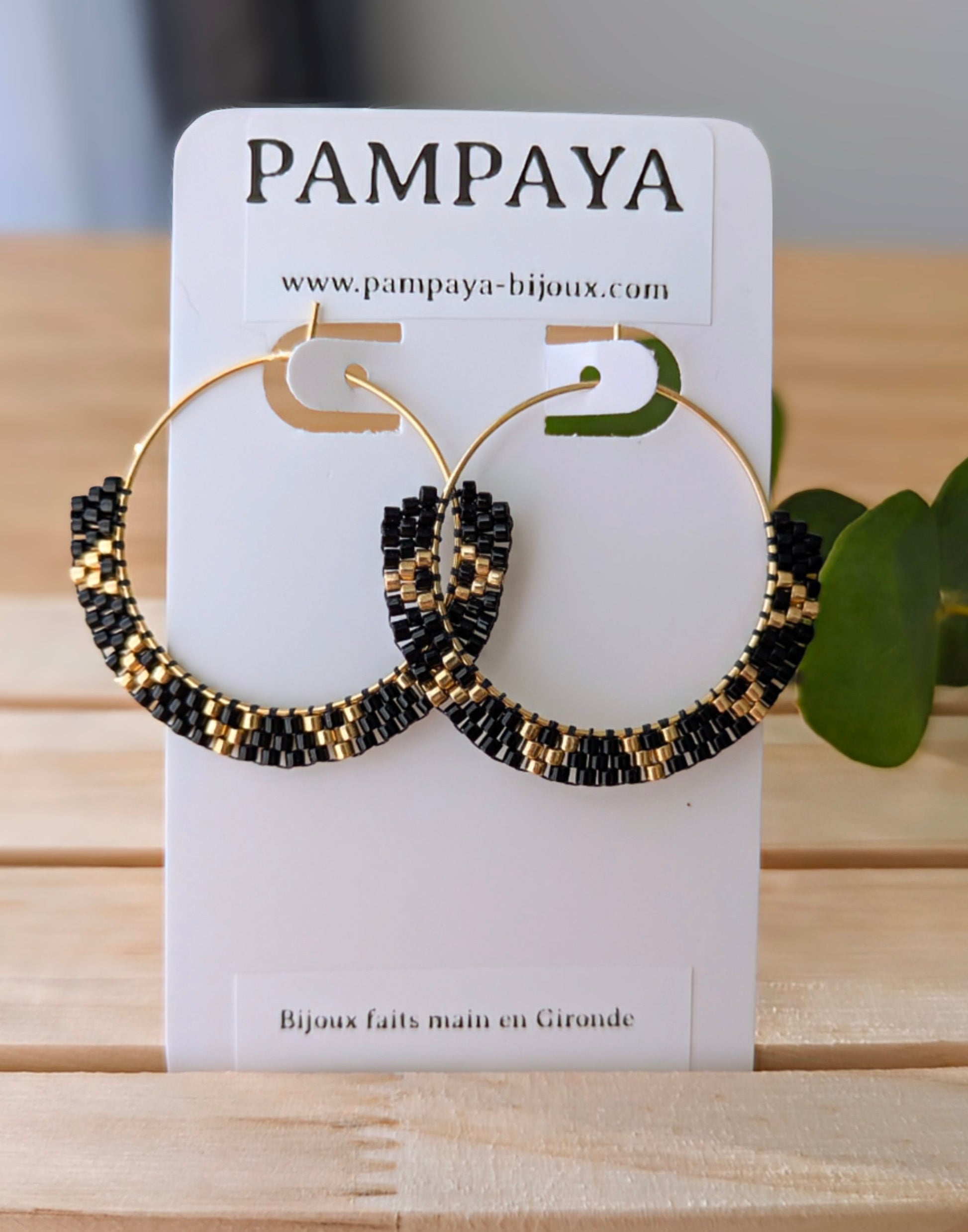 créoles noires et dorées en acier inoxydable présentées sur carton à bijoux avec inscription : "Pampaya - Bijoux faits main en Gironde"