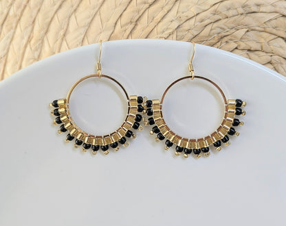 Boucles d'oreilles créoles noires et dorées exposées sur fond blanc