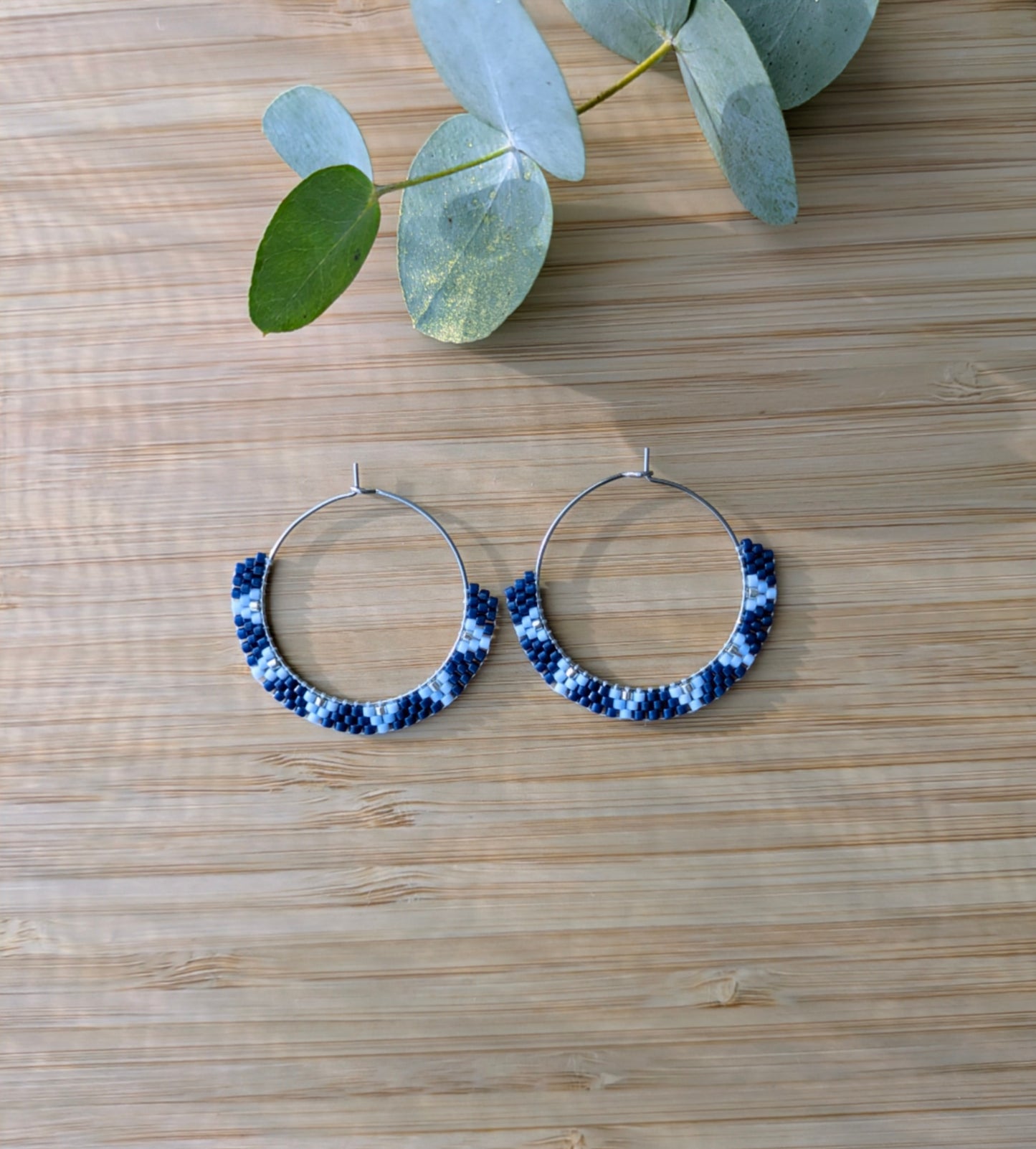 Créoles tissées main en perles bleues posées sur planche en bambou