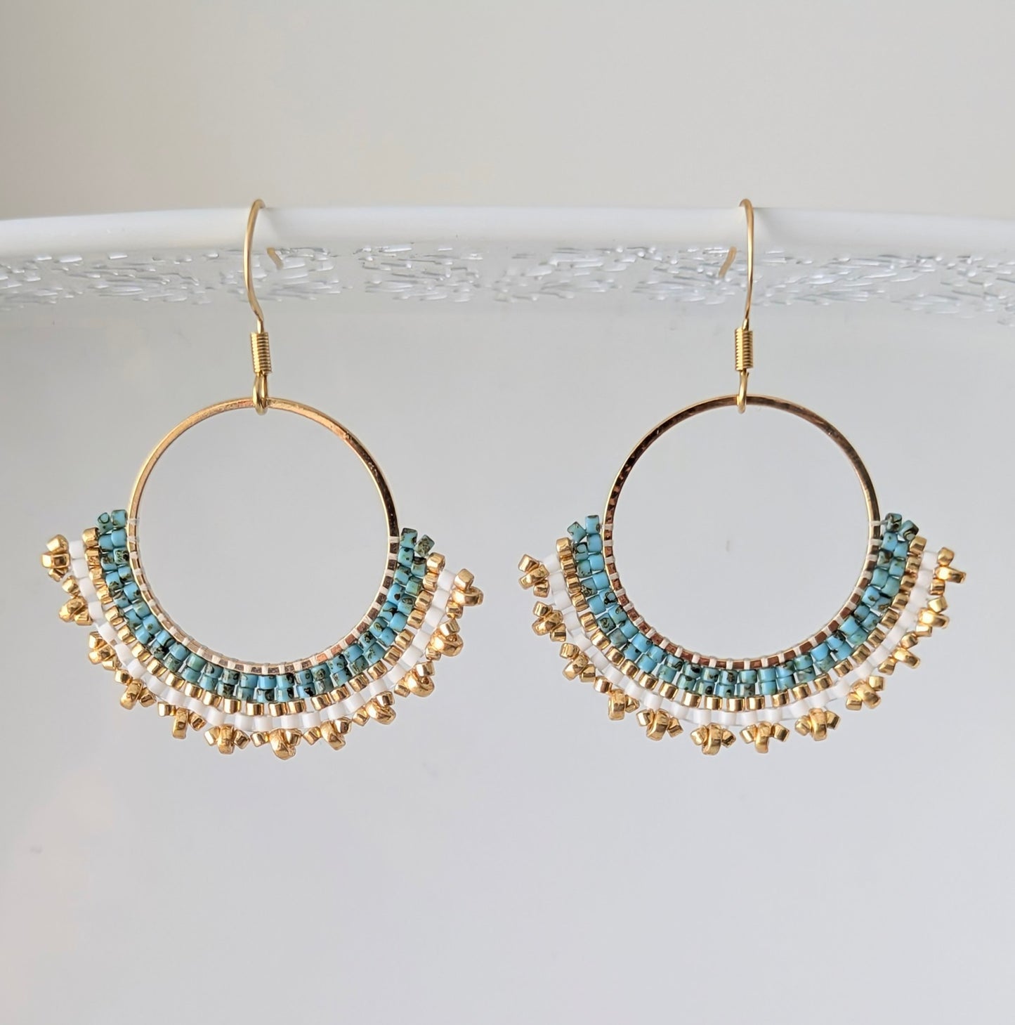 Vue détaillée du tissage artisanal des créoles pendantes en perles de verre bleues et dorées