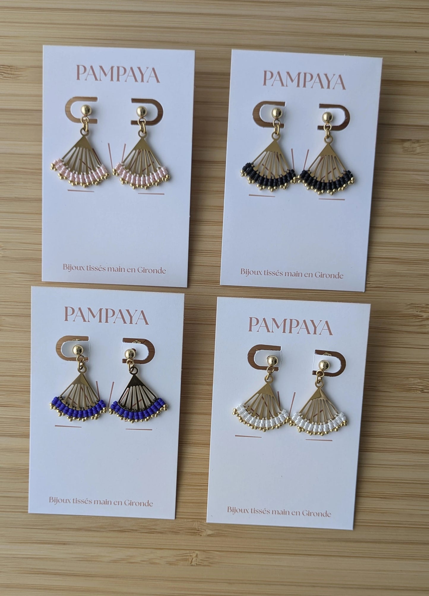 Quatre couleurs de boucles Lola présentées sur un support bijou : en perles roses, noires, bleues et blanches