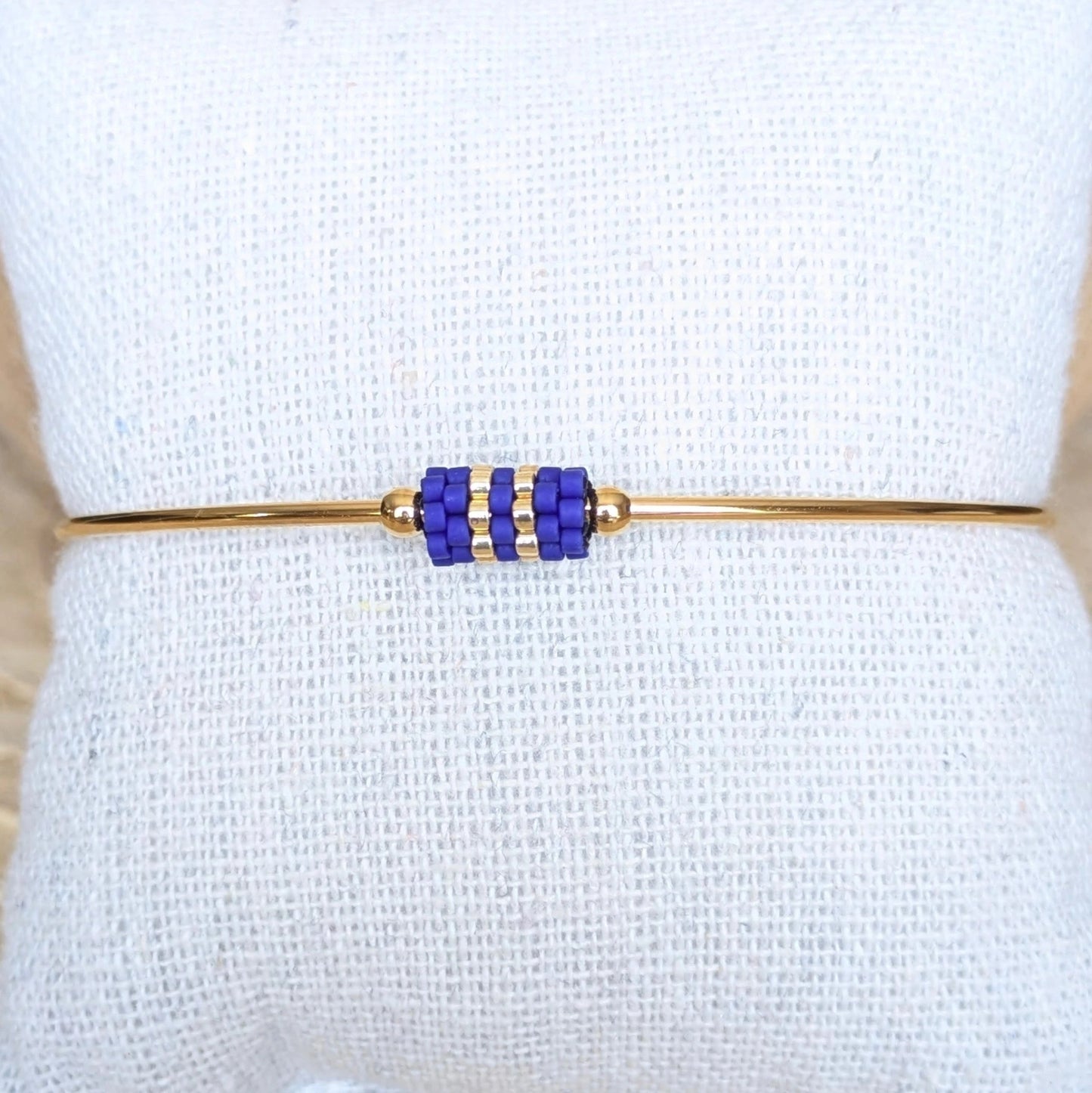 Gros plan sur bracelet jonc doré orné d'un tissage de perles bleues - Bijou présenté sur un coussin