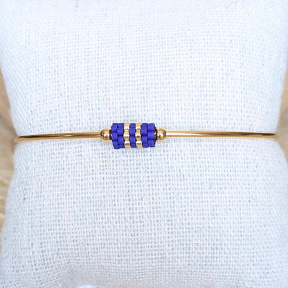 Gros plan sur bracelet jonc doré orné d'un tissage de perles bleues - Bijou présenté sur un coussin