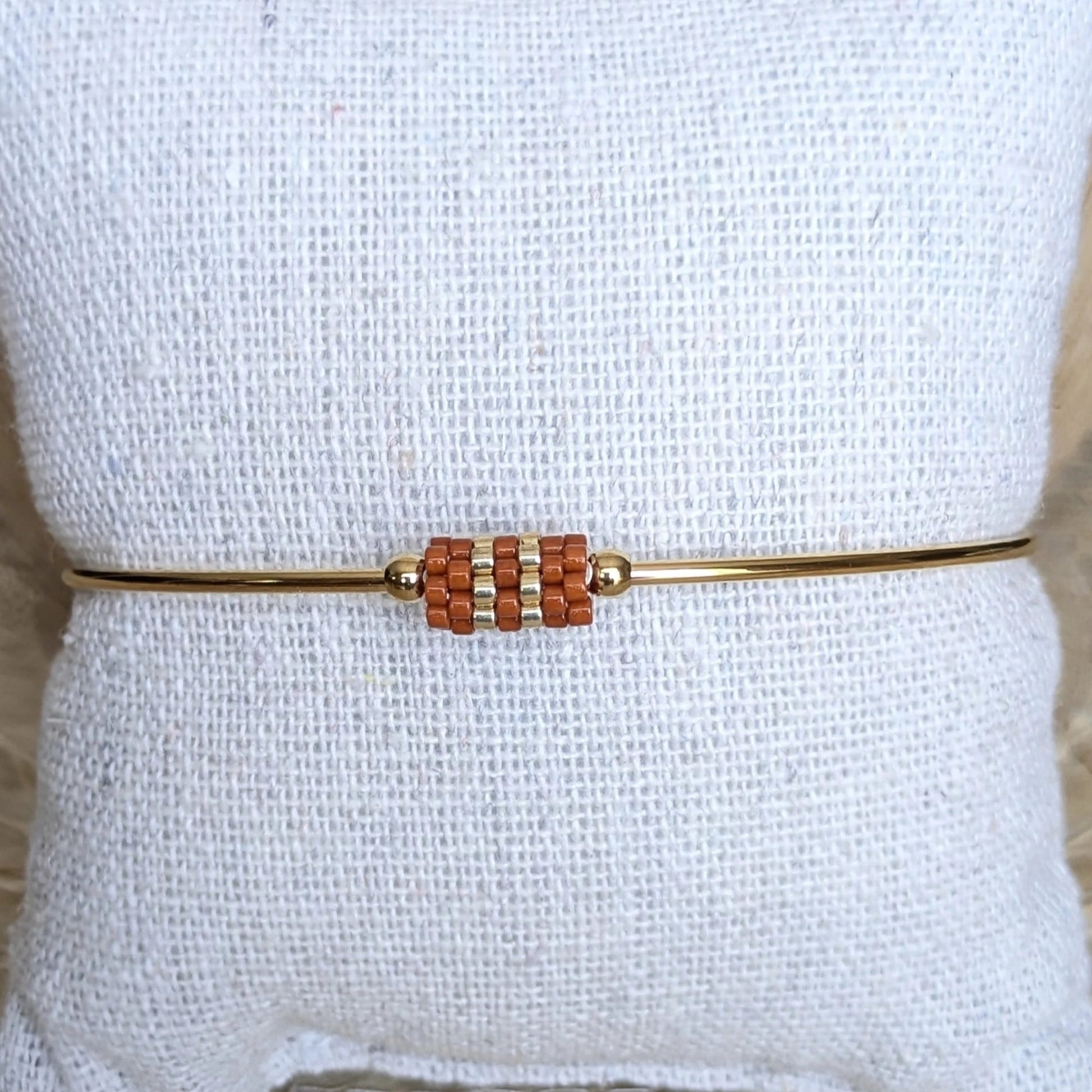 Gros plan sur jonc doré orné d'un tissage de perles couleur terracotta