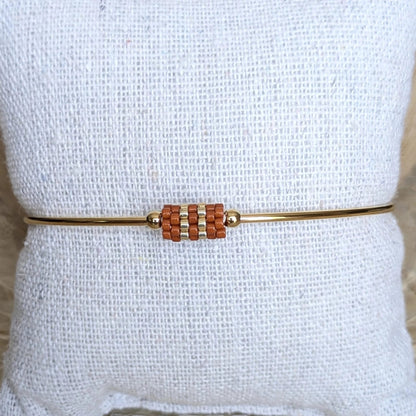 Gros plan sur jonc doré orné d'un tissage de perles couleur terracotta