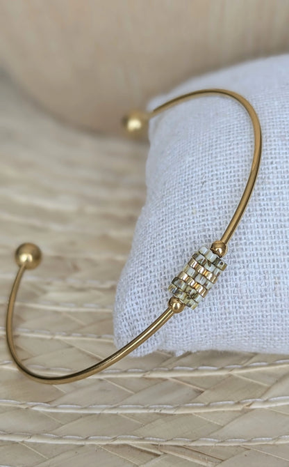 Bracelet jonc doré avec tissage de perles Yellow Picasso présenté sur coussin dans décor bohème