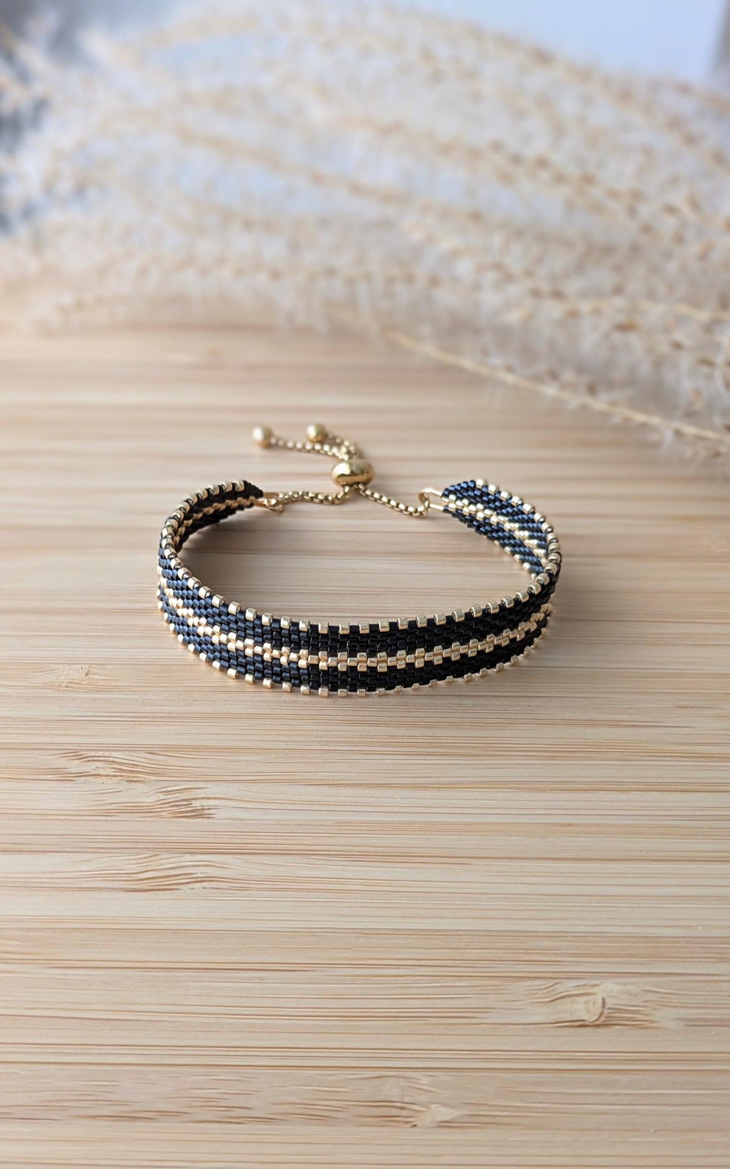 bracelet tissage peyote en perles noires et dorées sur planche en bambou