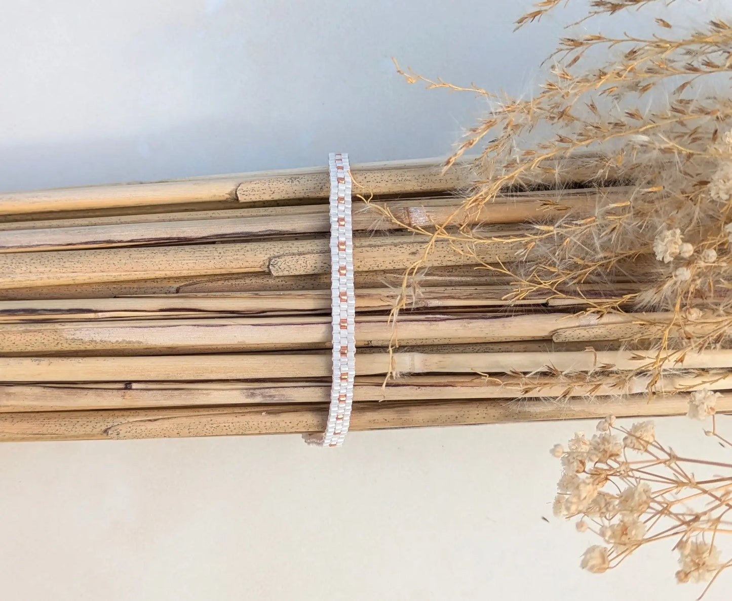 Bracelet tissé fin en perles de verre blanches et cuivrées sur fagot de bambous dans décor bohème