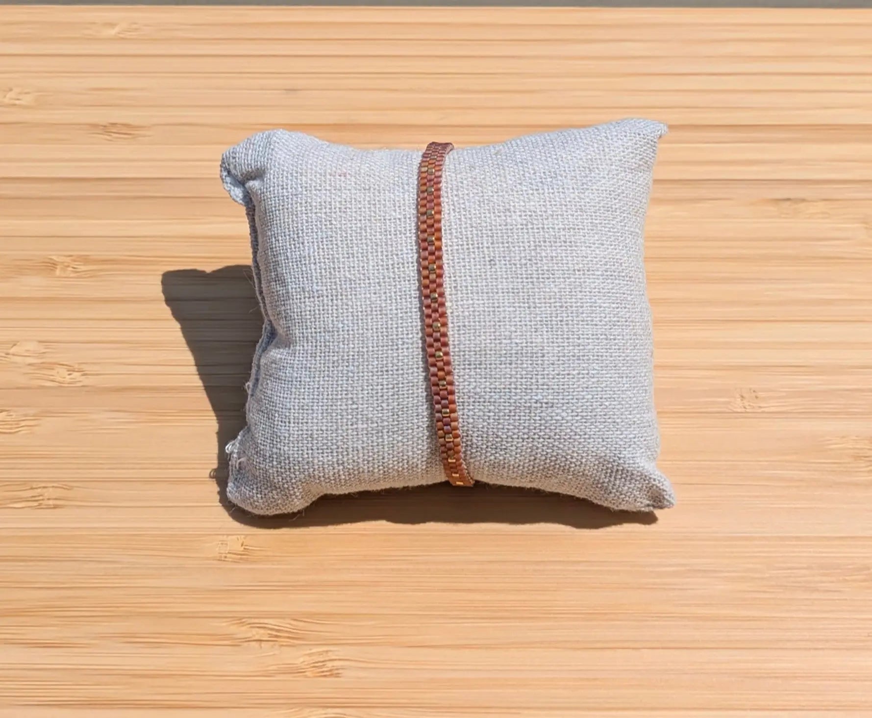 Bracelet artisanal tissé fin en perles miyuki rouge topaze présenté sur un coussin au soleil