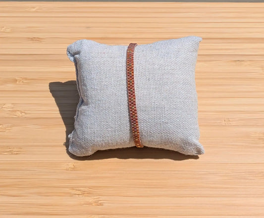 Bracelet artisanal tissé fin en perles miyuki rouge topaze présenté sur un coussin au soleil